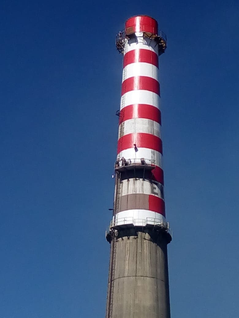 Chimenea de fundición ENAMI pintada a franjas rojas y blancas contra cielo azul